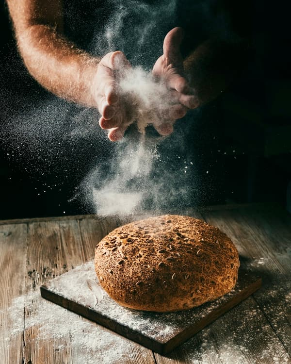 Bäcker bestäubt ein Brot mit Mehl